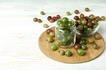 Board with jar and bowl of gooseberry on white wooden background