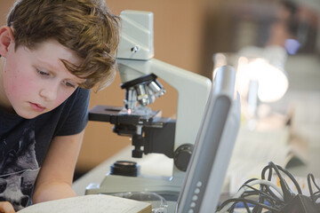 Boy student conducting scientific experiment at microscope and computer in laboratory classroom