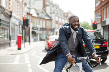 Playful young businessman commuting, riding bicycle on urban street