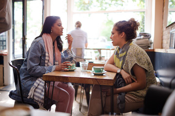Fototapeta premium Young women friends talking and drinking cappuccinos at cafe table