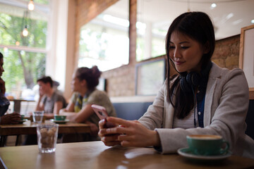 Young woman with headphones texting with cell phone and drinking coffee at cafe table