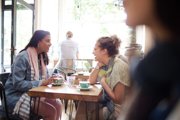 Young women friends talking and drinking cappuccinos at cafe table