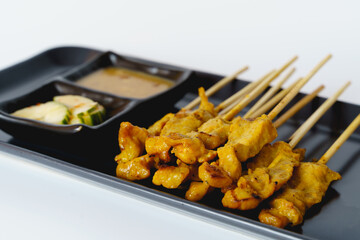 Pork satay with side dish and peanut dipping sauce in a black plate isolated on white background.