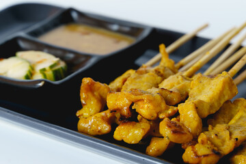 Pork satay with side dish and peanut dipping sauce in a black plate isolated on white background.