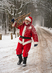 Christmas holiday. Winter vacation. Santa Claus in a traditional red costume walks along the road in a snowy forest with a sleigh in his hands.