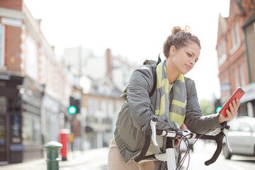 Young woman commuting on bicycle, texting with cell phone on sunny urban street