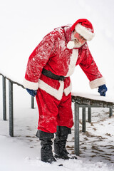 Christmas holiday and active lifestyle. Santa Claus in red traditional costume standing in front of a trampoline in a winter snowy park