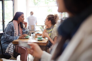 Young women friends talking and drinking cappuccinos at cafe table