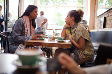 Young women friends talking and drinking cappuccinos at cafe table