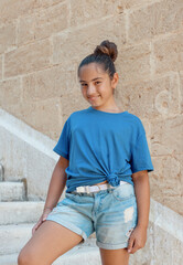 Smiling girl kid wearing t-shirt and shorts stays on stone stairs