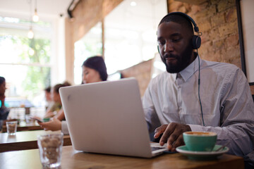 Man with headphones using laptop and drinking coffee in cafe