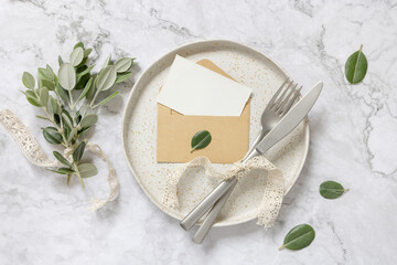 Blank paper card in envelope on plate with eucalyptus branches