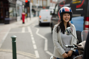Smiling young woman on motor scooter talking to friend on sunny urban street