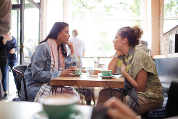 Young women friends talking and drinking cappuccinos at cafe table