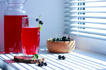 black currant juice with a glass glass on the window in the shade of the blinds, berries, summer soft drinks, healthy food