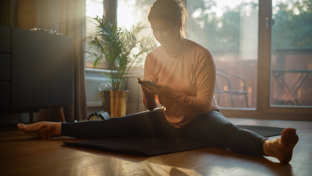 Beautiful Girl Using Smartphone to Help with Fitness Workout at Home. Smiling Woman Using Fitness Tracker, Yoga Exercises Application, Browsing Online Health Articles, Posting on Internet - Powered by Adobe