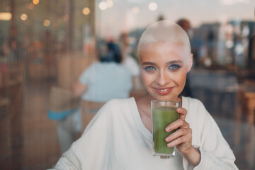 Portrait of young smiling millenial european short haired woman looking through glass with green smoothie at cafe. Beautiful happy blonde girl indoor.