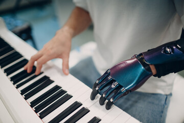 Young disabled man playing on piano electronic synthesizer with artificial prosthetic hand in music...