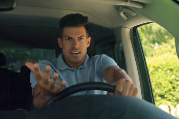 Stressed angry man in driver's seat of modern car, view through windshield