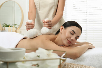 Fototapeta na wymiar Young woman receiving herbal bag massage in spa salon
