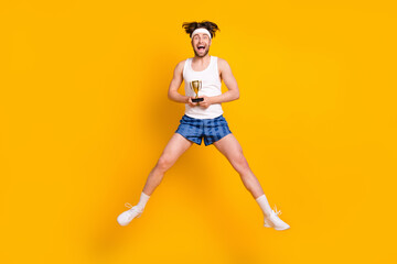 Fototapeta na wymiar Full length body size view of attractive cheerful sportive guy jumping holding cup isolated over bright yellow color background