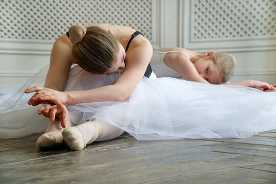 Two ballerinas lie on the floor. Little and adult ballerina