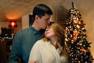Fototapeta premium Beautiful middle aged caucasian couple posing in new year interior with a christmas tree and garlands. Selective soft focus, film grain effect