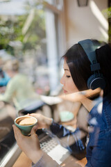 Pensive young woman listening to music with headphones looking away at cafe window