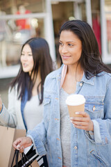 Smiling women friends walking arm in arm along storefront with coffee and shopping bags
