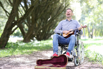 Fototapeta premium Disabled man in wheelchair plays guitar in park and makes money