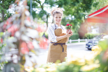 Fototapeta premium Female florist checking plants at sunny flower shop storefront