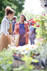 Fototapeta premium Female florist helping pregnant shopper at flower shop storefront