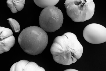 Grayscale shot of garlic, tomatoes, and eggs on a surface