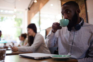 Young man with headphones drinking coffee in cafe