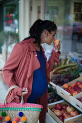 Pregnant woman shopping, smelling fruit at market storefront