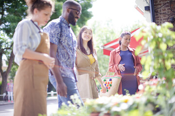 Female florist helping friends at sunny flower shop storefront