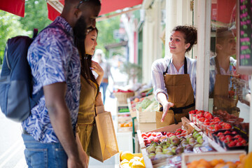 Obraz premium Female worker helping young couple shopping for fruit at market storefront
