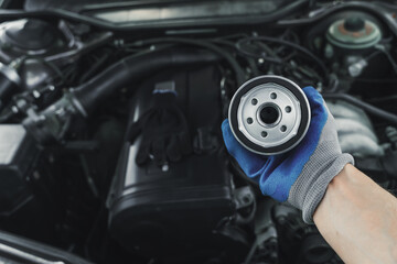 Replacing the oil filter. Car engine maintenance mechanic holds an oil filter in his hand against the background of an open car hood