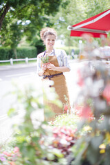 Female florist checking plants at sunny flower shop storefront