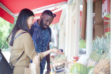 Young couple shopping for produce, looking at prices at outdoor market