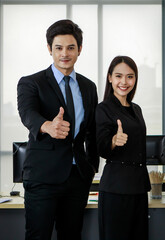 Asian young smart confident professional businessman and businesswoman colleague in formal business suit standing smiling look at camera pose show thumbs up together in front working desk in office