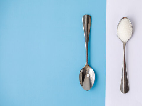 Choice of Sweetener in tablets or regular sugar. Alternative to sugar for diabetics. Sugar-replacement tablet and sugar in tea spoons lying in opposite directions on blue white background. Horizontal