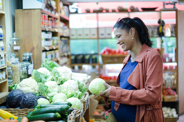 Pregnant woman shopping for cabbage in grocery store