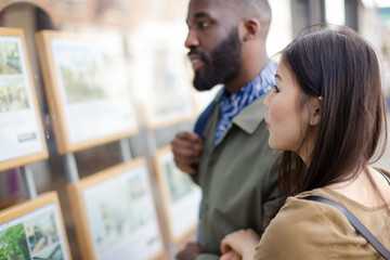 Young couple browsing real estate listings at storefront