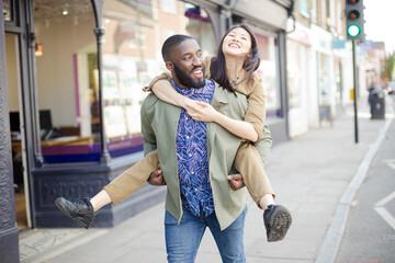 Playful young couple piggybacking on urban street