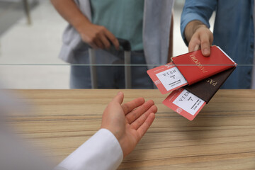 Man giving passports with tickets to agent at check-in desk in airport, closeup