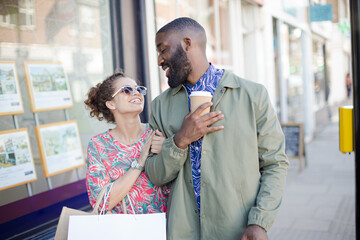 Affectionate young couple with coffee and shopping bag outside storefront