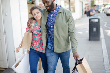 Affectionate young couple with shopping bag walking along storefront