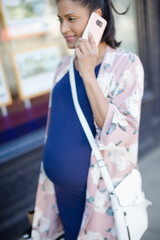 Fototapeta premium Pregnant woman talking on cell phone, walking along urban storefront