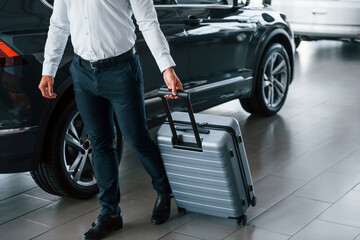 Obraz premium Conception of tourism. Man in formal clothes is with luggage indoors near the car